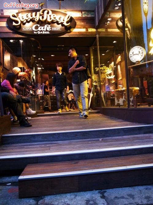 台北 StayReal Café——旅人归家
地址：台北敦化南路1段177巷21号
StayReal Café是阿信与不二良，继服饰店后，另一个跨足的品牌事业。爱喝咖啡，每天至少一、两杯纯美式咖啡的阿信和他的朋友们继续着年少时的梦想——开咖啡店。除非手上有正确的地址，若只是站在街头往巷内看，可能会错过它，唯有进入巷弄里，才会被它３米高的横式店招吸引，一旁还有难得的绿荫，底下的橱窗中，展现着老板阿信与他高中好友不二良对“家”的坚持。
StayReal Café是一家营造旅人回家感觉的咖啡馆。进入店内，就能感受到这里艺术味浓厚的氛围，右面墙上，挂着多幅村上龙与香港艺术家Molly by Kenny的作品，左边陈列着“一克拉的梦想”艺术展周边商品，让展出时没到的人，可在这里挑选。连菜单也编排得像一本精美图文书，从试营运到正式开店，它已被翻得快变形了。让员工们感动的是，店里的所有陈设，举凡画作、皮制复古沙发、木箱或皮箱，到最里面的个人珍藏柜里的宝物，甚至只是灯光角度，阿信都会自己动手调整。也就是说，也许你坐的位子，可能是大明星前一晚来时调整过的！